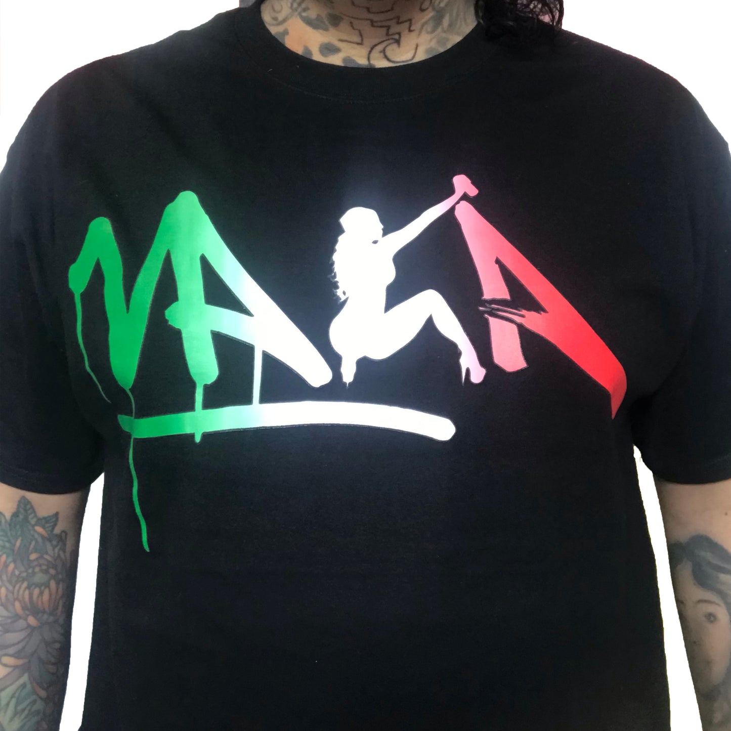 A black crew neck t-shirt with a graphic design featuring the name 'VAKA' in stylized graffiti tag font, filled with the colors of the Mexican flag, and a silhouette of a spray-painting pin-up figure.