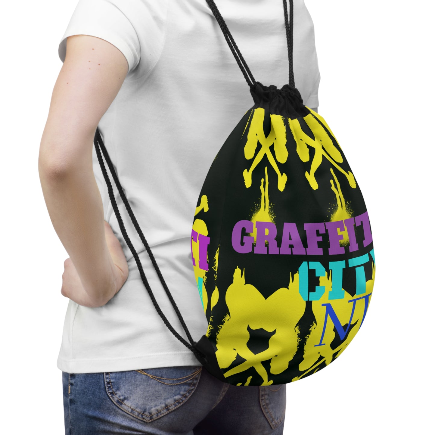 A person wearing a white t-shirt and blue jeans is shown from the back, carrying a black drawstring backpack. The backpack features a bold graphic design with yellow graffiti-style paint splatters, a skull motif, and text reading 'GRAFFITI CITY' in purple and teal.