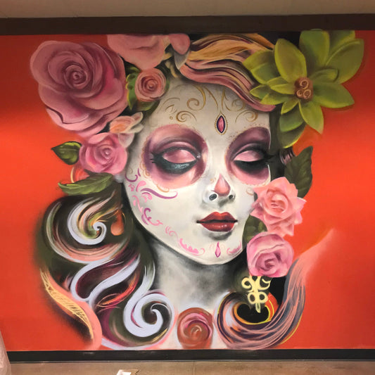 Artistic depiction of a woman with sugar skull makeup and floral elements on an orange background