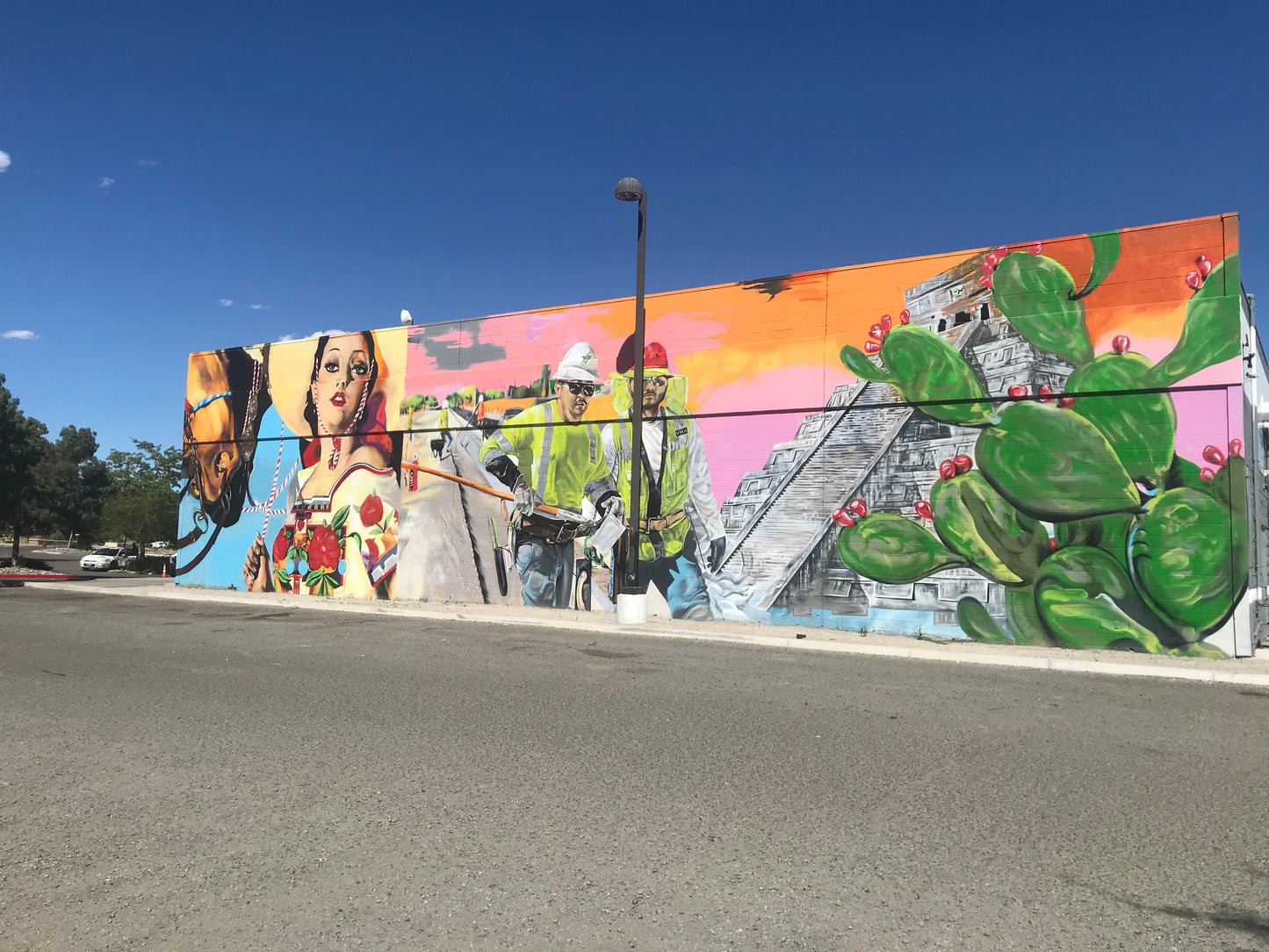 Colorful mural on a wall with various elements including a pyramid and people, set against a clear blue sky.