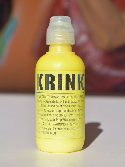 A yellow bottle of Krink K-60 squeeze marker with black text on it, set against a colorful background.