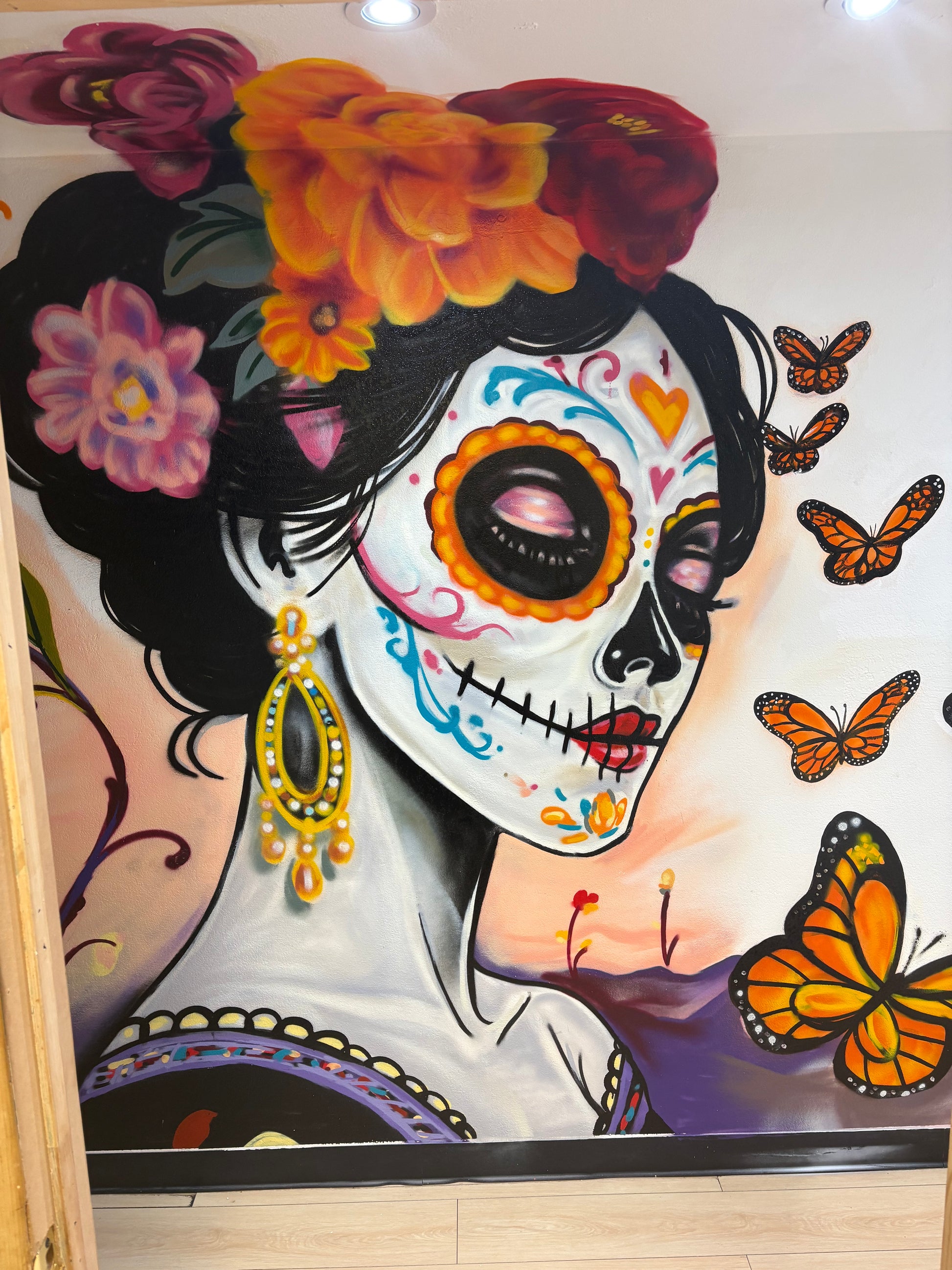 Mural of a stylized skull with colorful flowers and butterflies on a wall.