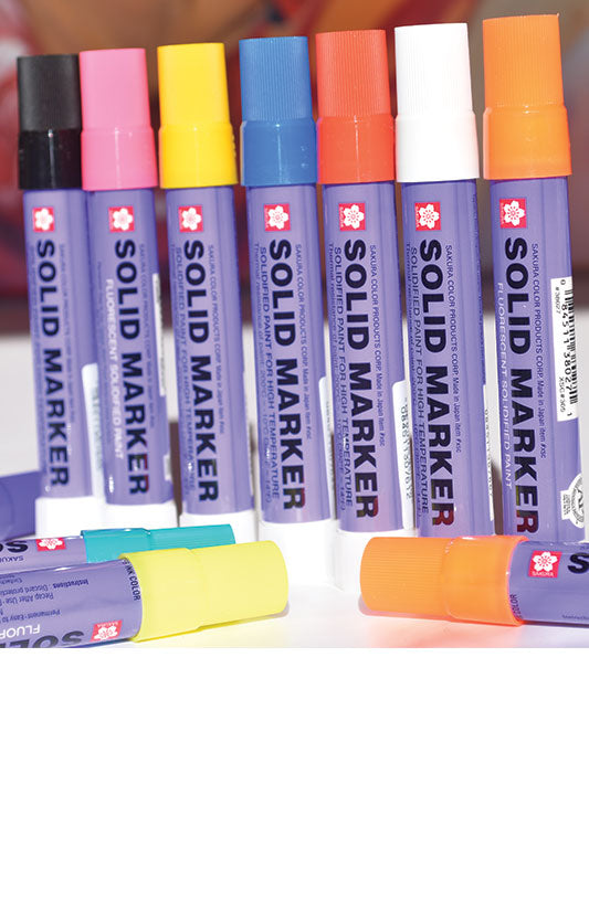 A collection of Sakura Solid Paint Markers in various colors, with twist-top caps.