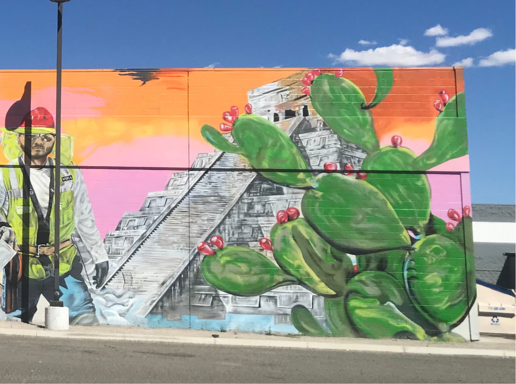 Mural with a person in a green jacket, cacti, and pyramid design on a building.