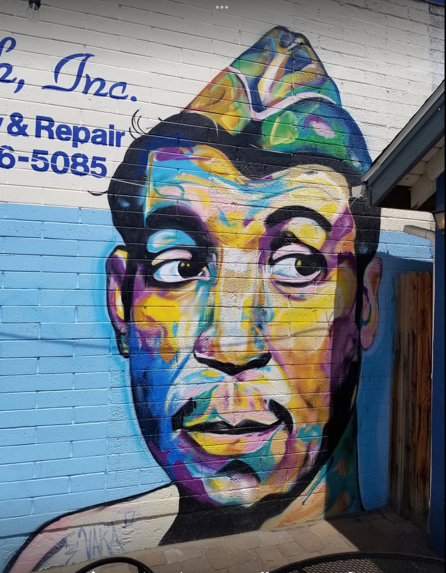 Colorful mural of a face on a brick wall with contact information above.
