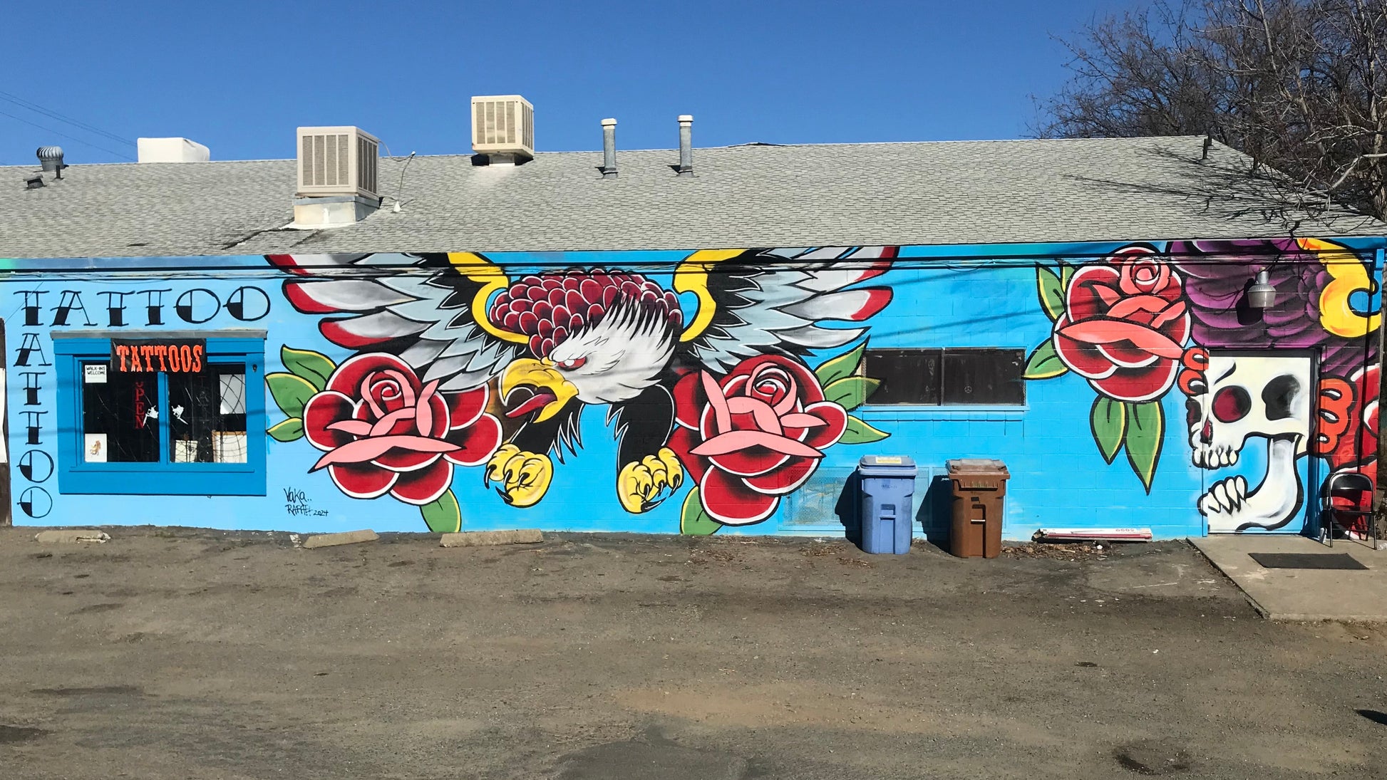 Tattoo parlor with a colorful mural on the wall featuring an eagle, roses, and skulls.