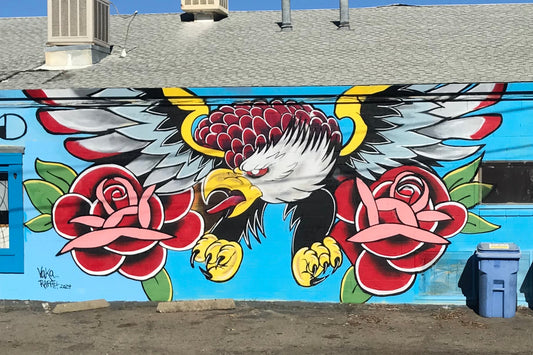 Mural of an eagle with roses on a blue background, featuring a trash can in the foreground.