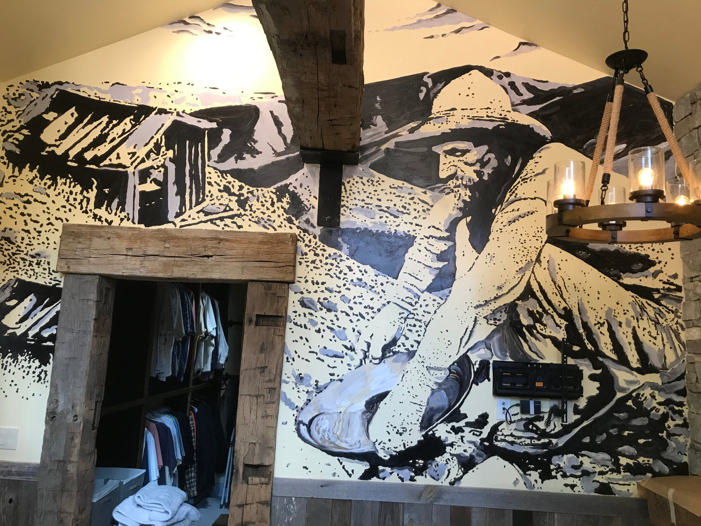 Mural of a person sitting on a rock with a scenic background in a room with wooden furniture.