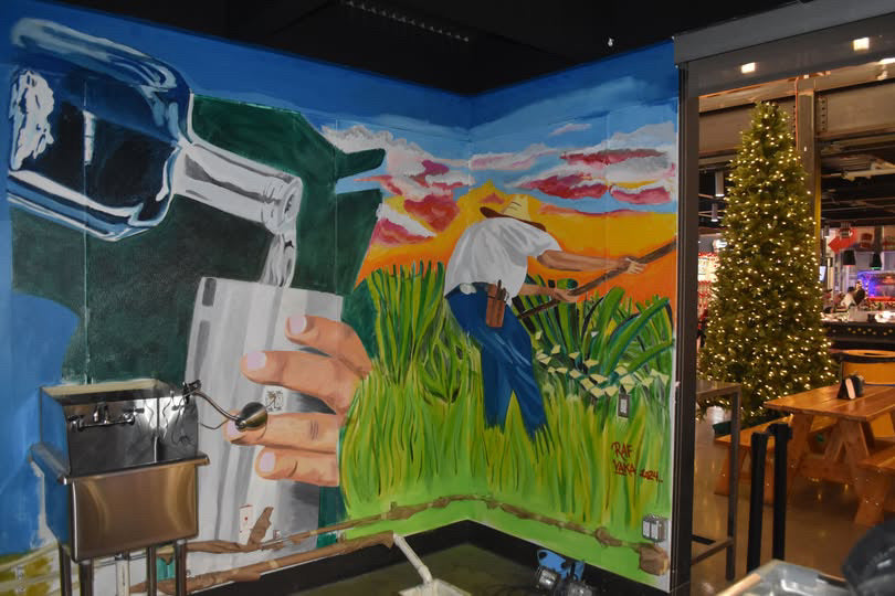 Mural of a hand holding a gun with a landscape and person in the background, inside a building.
