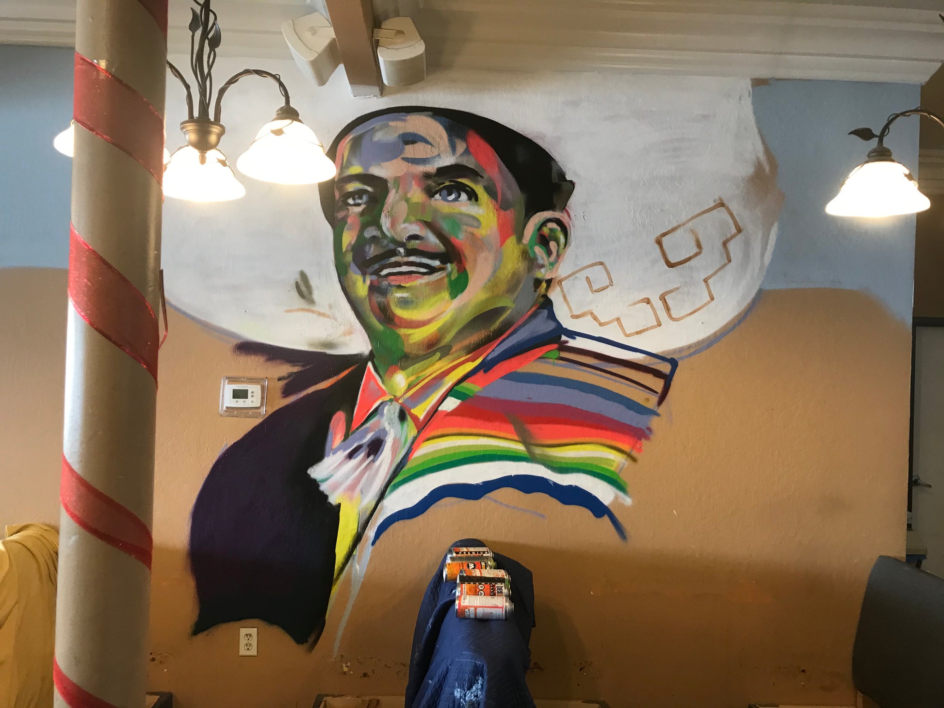 Mural of a person with a rainbow scarf on a wall with lights above.